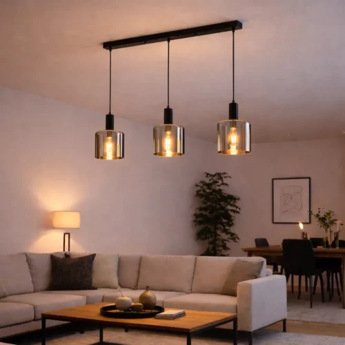Suspension lumineuse à trois abat-jour en verre transparent, éclairage chaleureux sur salon moderne avec canapé et table basse.