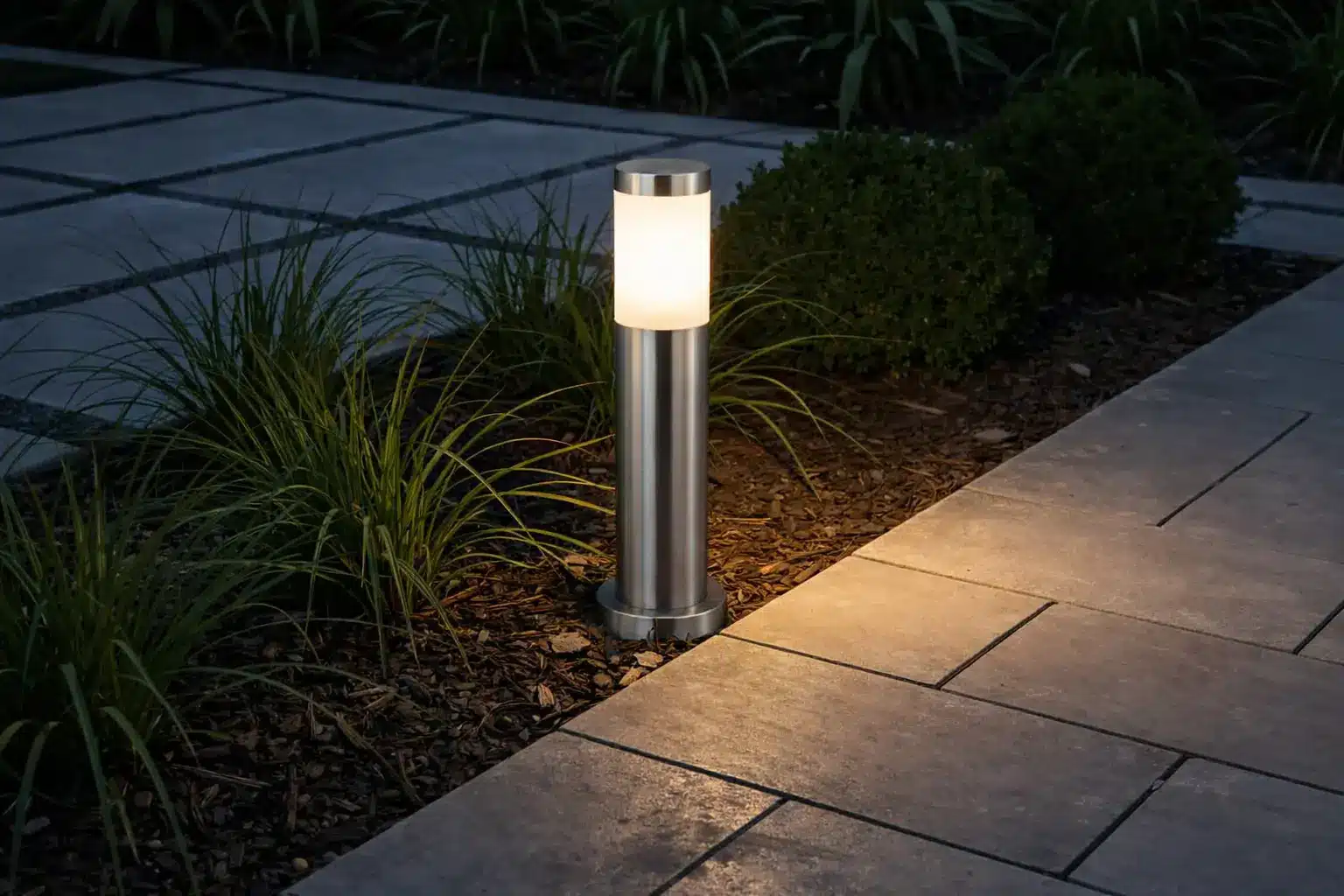 Lampe d’extérieur moderne en colonne inox, avec abat-jour oval translucide, éclairant gravier et pavage adjacent.