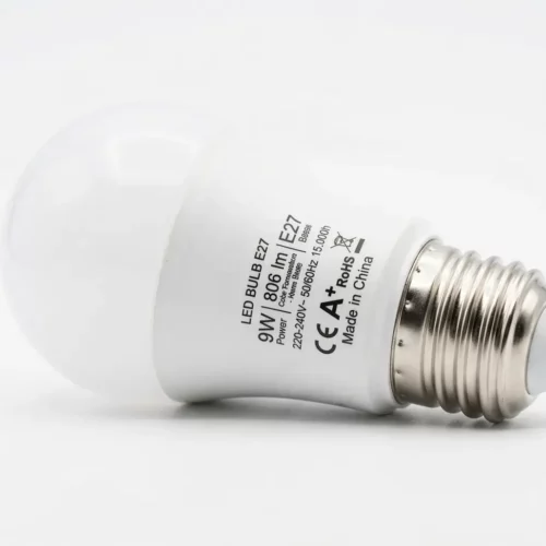 Ampoule LED E27 blanche, refroidie et inclinée sur fond blanc, inscription et norme CE/EA visibles sur le corps métallique.