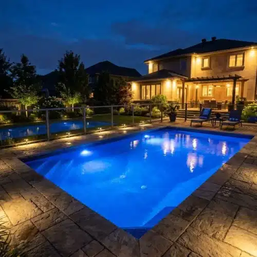 Éclairage piscine jardin : vue nocturne d’une piscine illuminée, entourée de terrasse en pierre et d’un jardin éclairé, avec maison lumineuse en arrière-plan. éspérons l’intégration: éclairage piscine jardin normes.