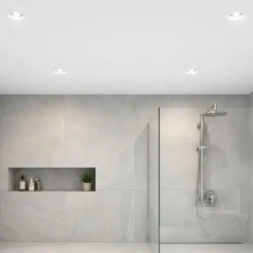 Éclairage salle de bain led : salle de bains moderne avec douche à porte vitrée, paroi en verre et murs en carreaux gris clair, affichant un éclairage encastré au plafond.