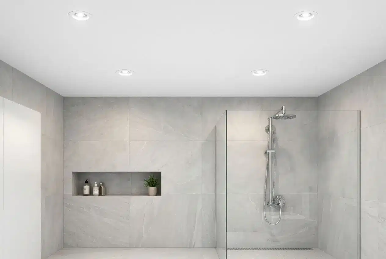 Éclairage salle de bain led : salle de bains moderne avec douche à porte vitrée, paroi en verre et murs en carreaux gris clair, affichant un éclairage encastré au plafond.